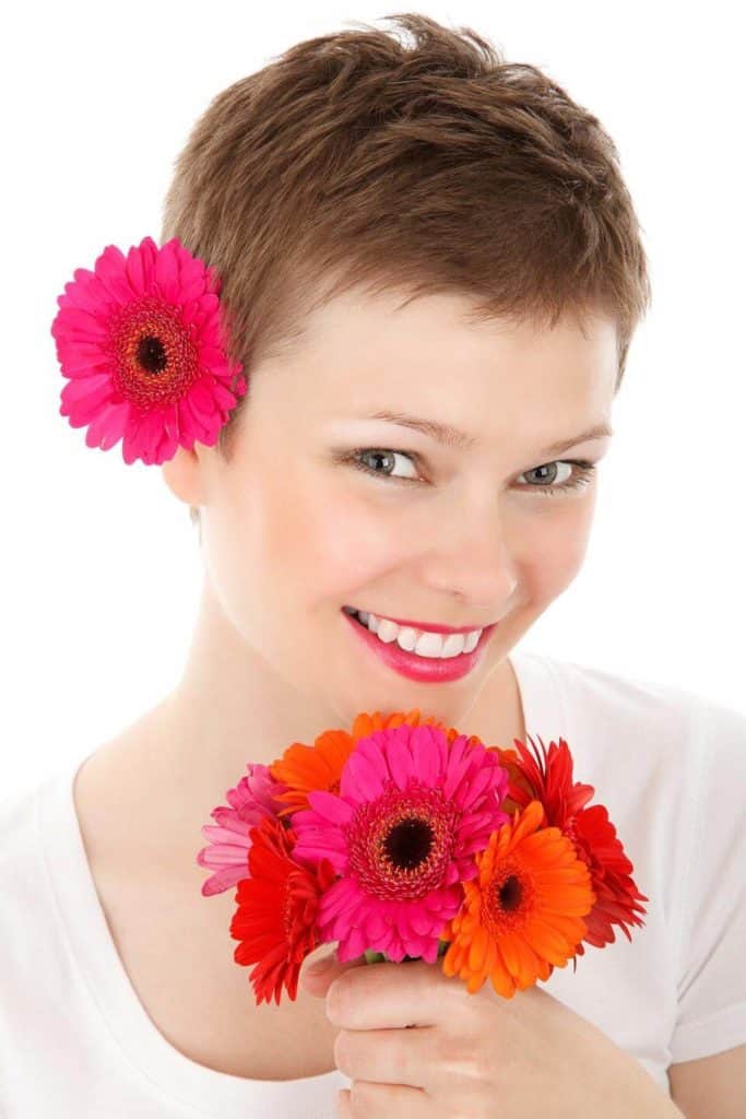 امرأة شعرها قصير تبتسم وتضع وردة على شعرها وتمسك باقة أزهار بيدها